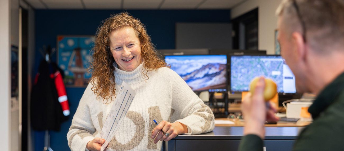 Collega’s in overleg op kantoor, met documenten en beeldschermen, informele werksfeer binnen het team.