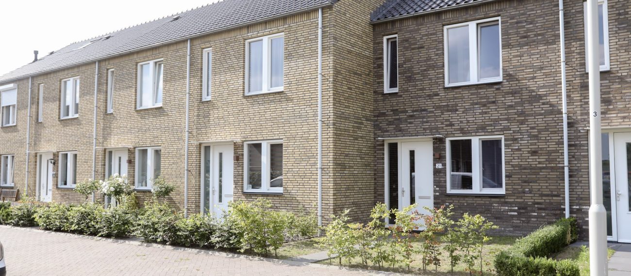 Rij moderne nieuwbouwwoningen met bakstenen gevels, witte kozijnen en kleine voortuinen in woonwijk