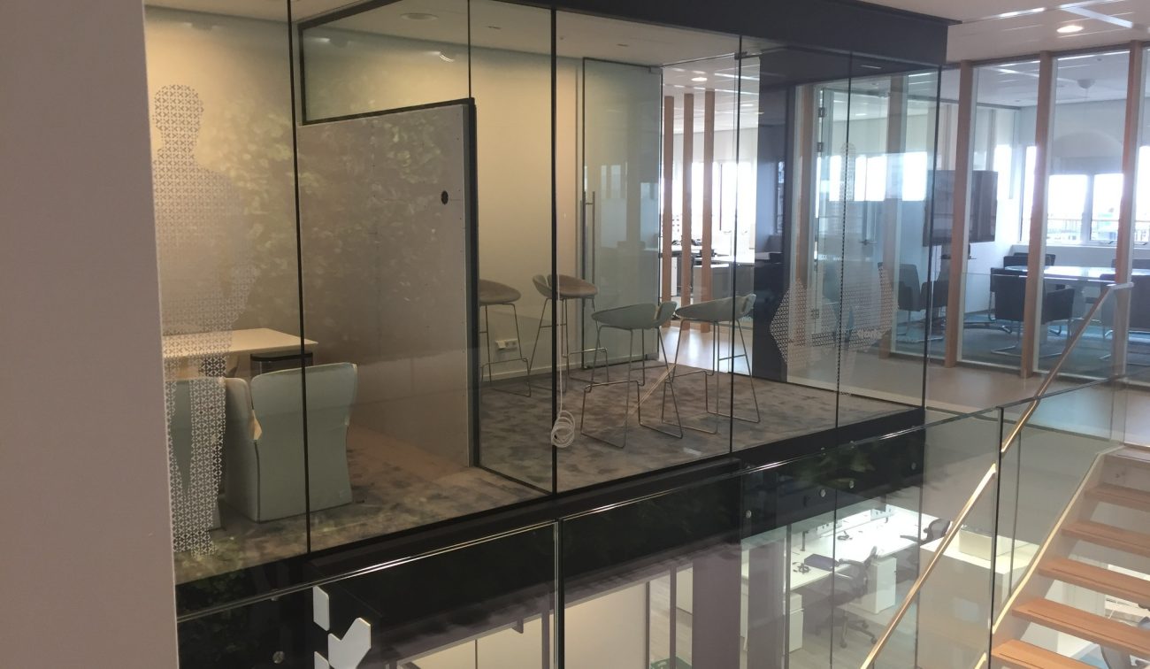 Modern kantoorinterieur met glazen vergaderruimtes, vide & glasbalustrade en houten trap met treden.