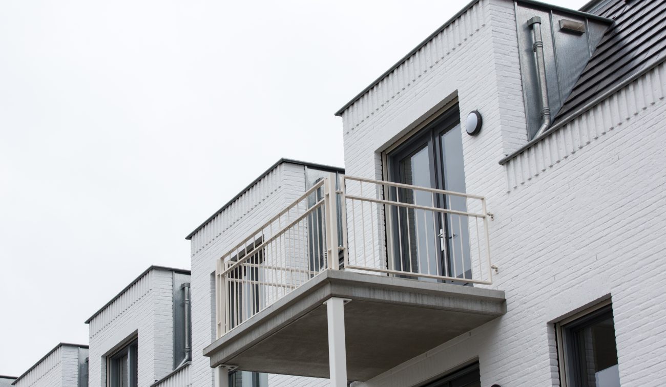 Hof te Berkel Horst – witgeschilderde bakstenen gevel met klein balkon op betonplaat, licht hekwerk en grijze openslaande deuren