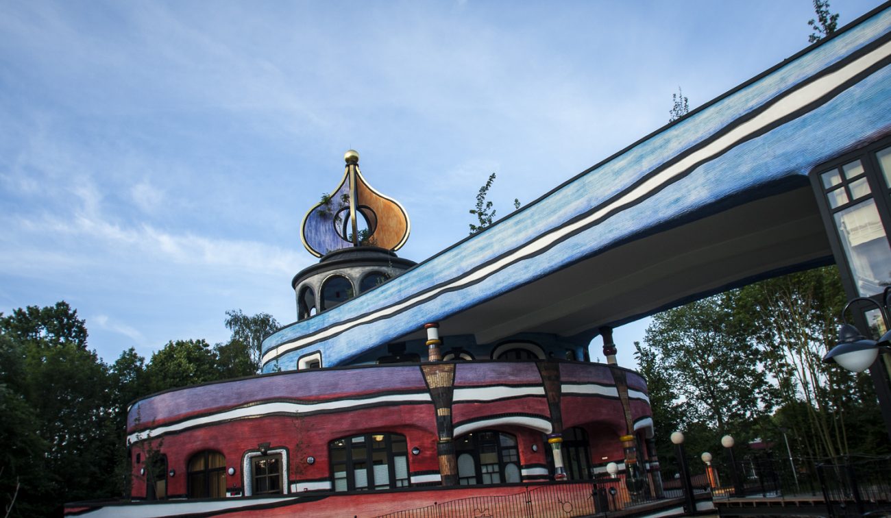 Ronald McDonald Kindervallei in Valkenburg met kleurrige Hundertwasser-gevel, goudkleurige ui-koepel en overkragende blauwe boog boven de ronde rode bouwdelen.