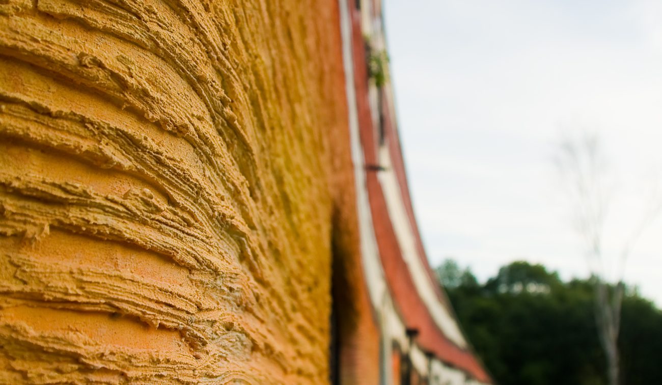 Close-up van de golvende, oranje stucgevel van de Kindervallei in Valkenburg met het gebouw in perspectief en groen ernaast.