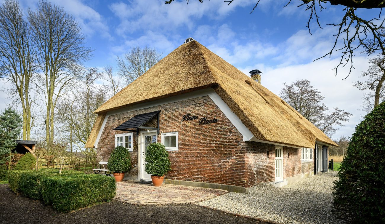 Gerestaureerde woonboerderij Naardermeer: baksteen, wit houtwerk, rieten dak en groene erfhaag