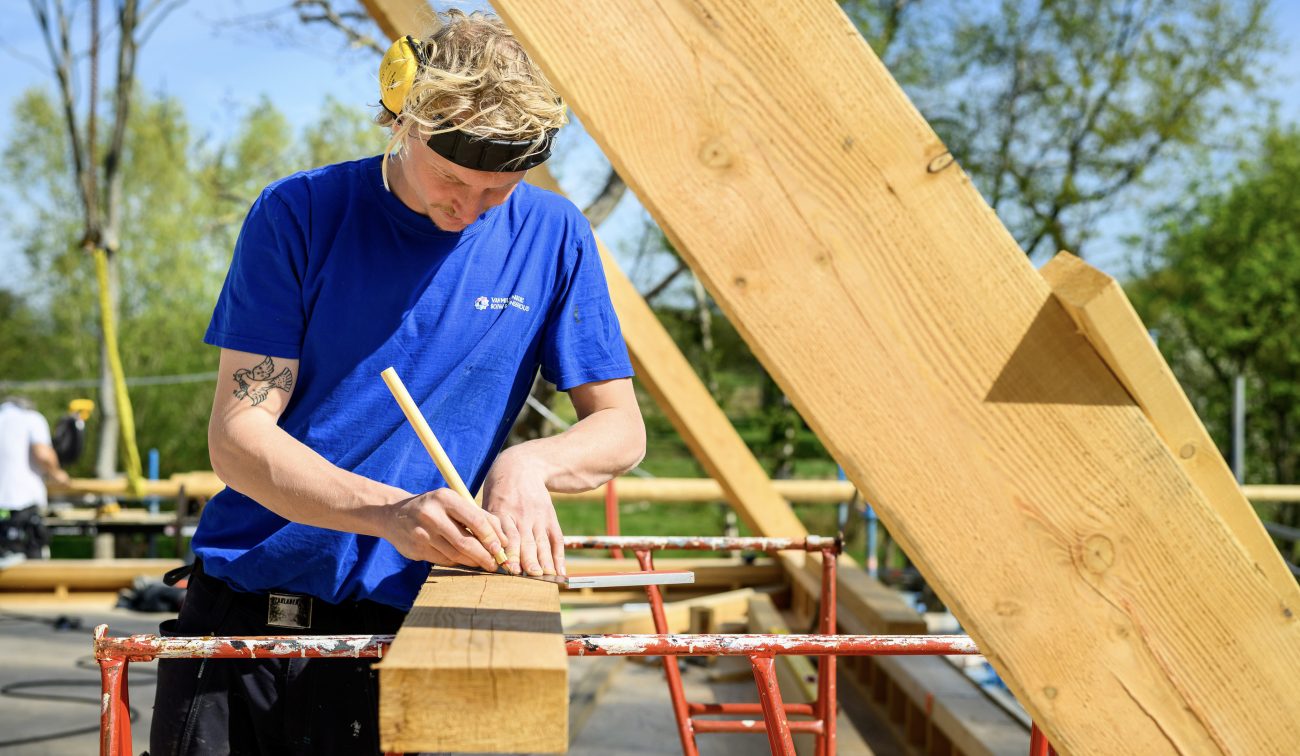 Timmerman markeert eiken balk met potlood; opbouw houten spant tijdens renovatie Naardermeer