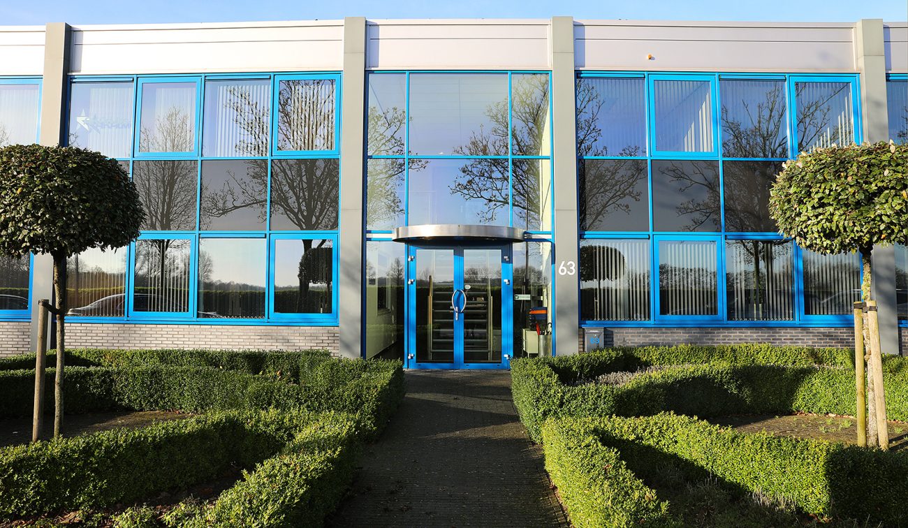 Moderne bedrijfsgevel met grote blauwe ramen, glazen entree en strak aangelegde groene tuin ervoor