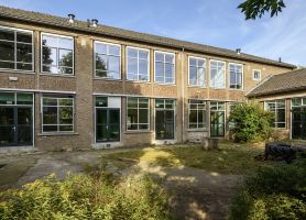 Renovatie De Fakkel Utrecht: klassenvleugel aan patio met veel glas, baksteenritme en groen