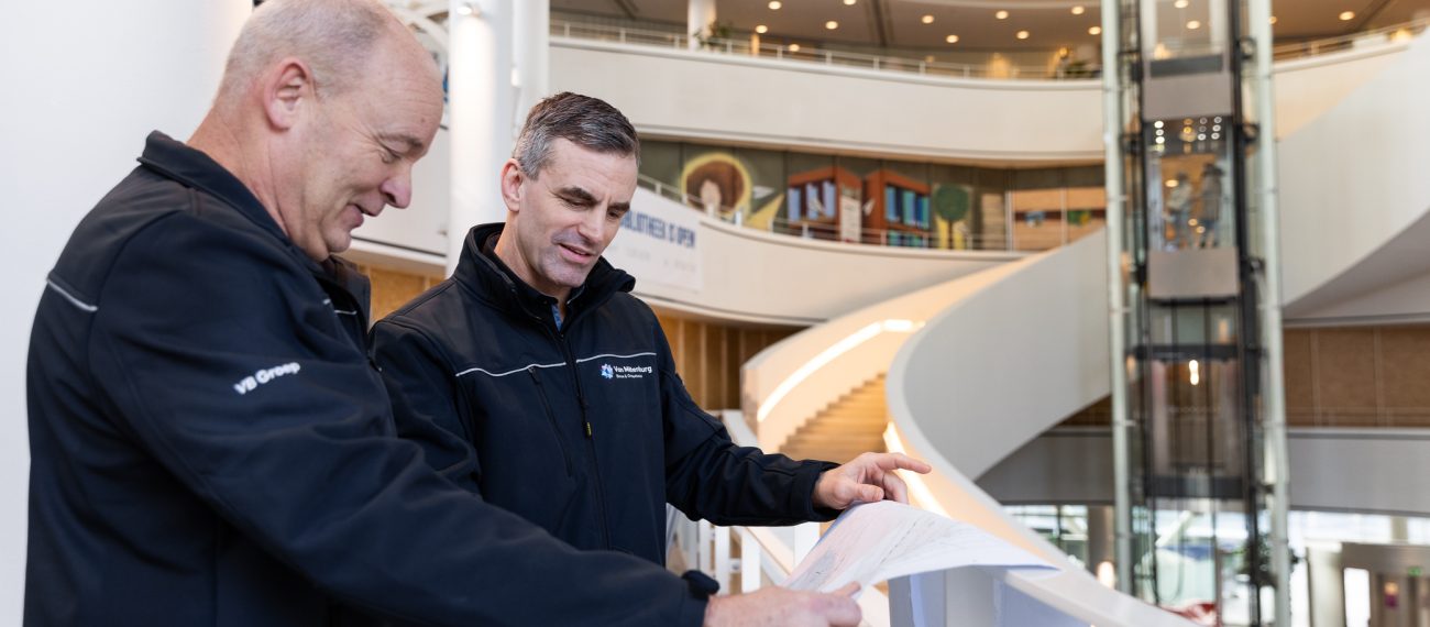 Technici bekijken bouwtekeningen in een modern atrium.
