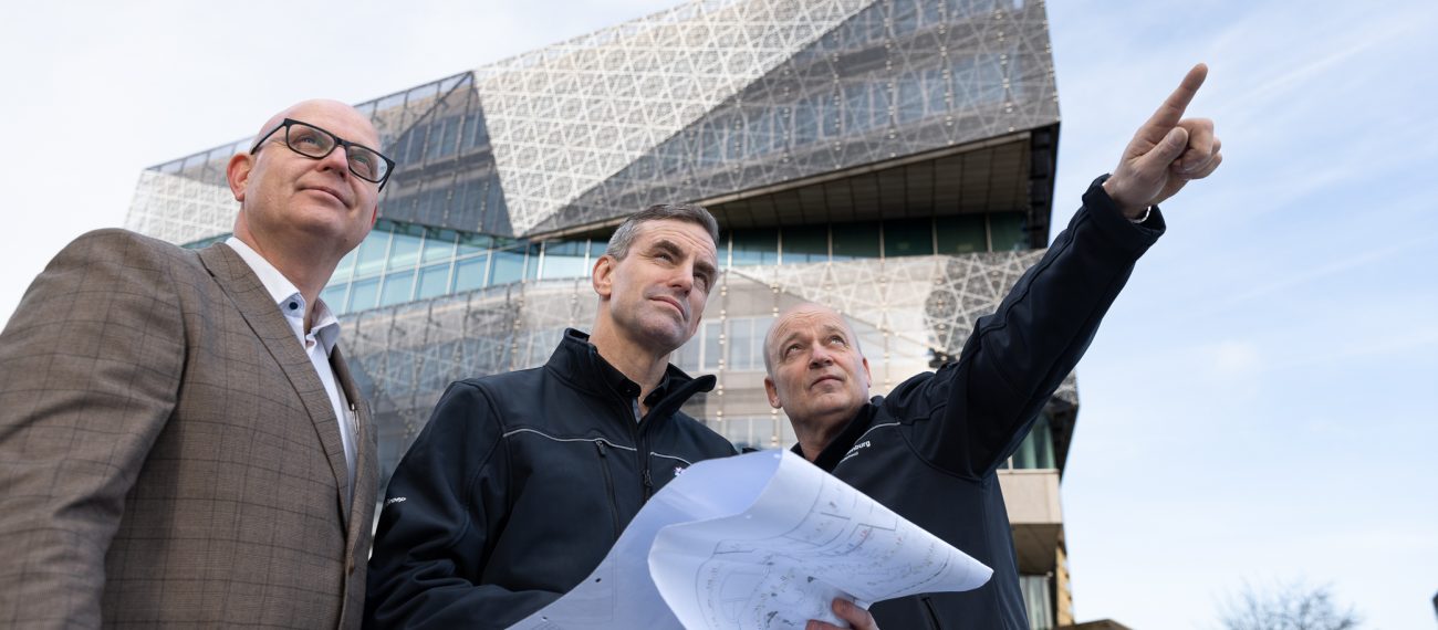 Drie professionals bekijken bouwtekeningen voor modern architectonisch gebouw en wijzen richting project
