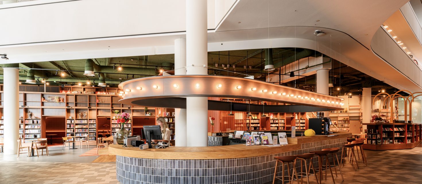 Moderne ontvangstzone met tegelbalie, brochures en open boekenkastruimte.