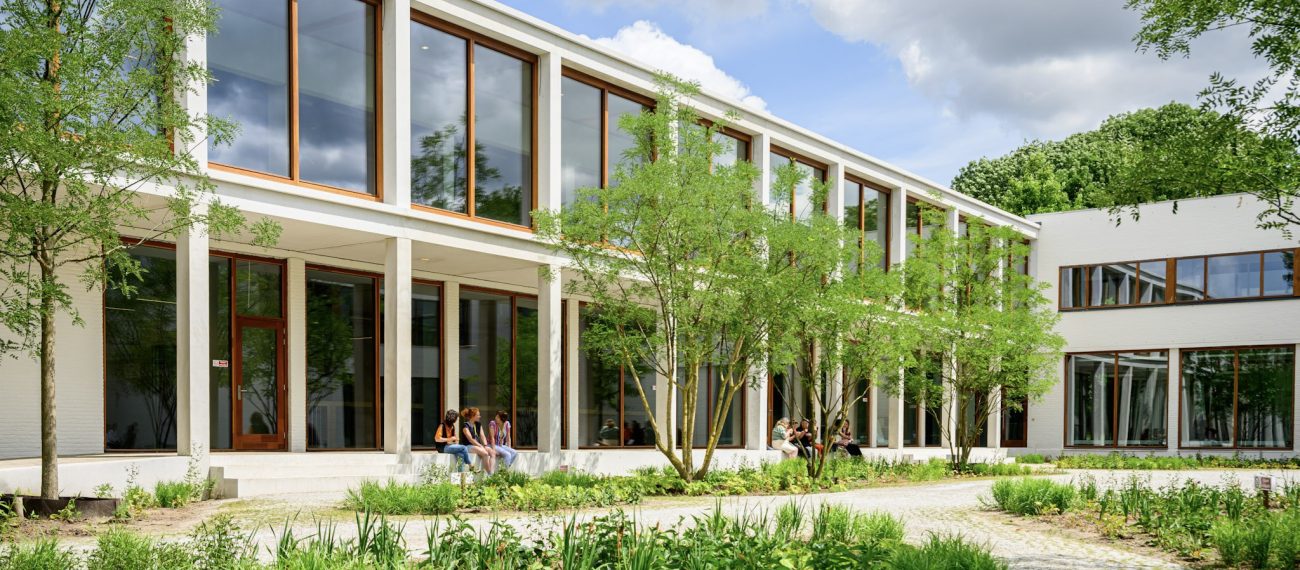 Transparante onderwijsgevel met veranda langs de patio; leerlingen relaxen tussen het groen.