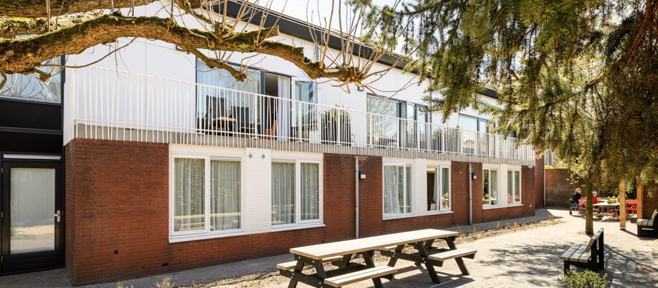 Renovatie en optopping Plataanlaan Baarn: woongebouw met balkonhekken, baksteen, tuin en oude bomen.