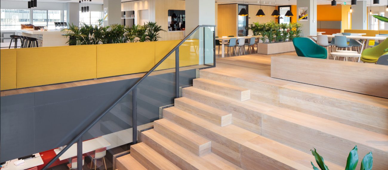 Renovatie kantoren stationsgebied Utrecht CS: interieur met houten tribunetrap, planten en werkcafé.