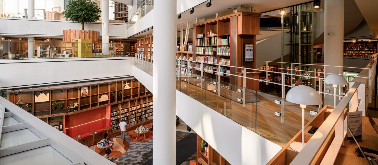 Lichte atriumbibliotheek met houten boekenkasten, glazen balustrades en witte kolommen.