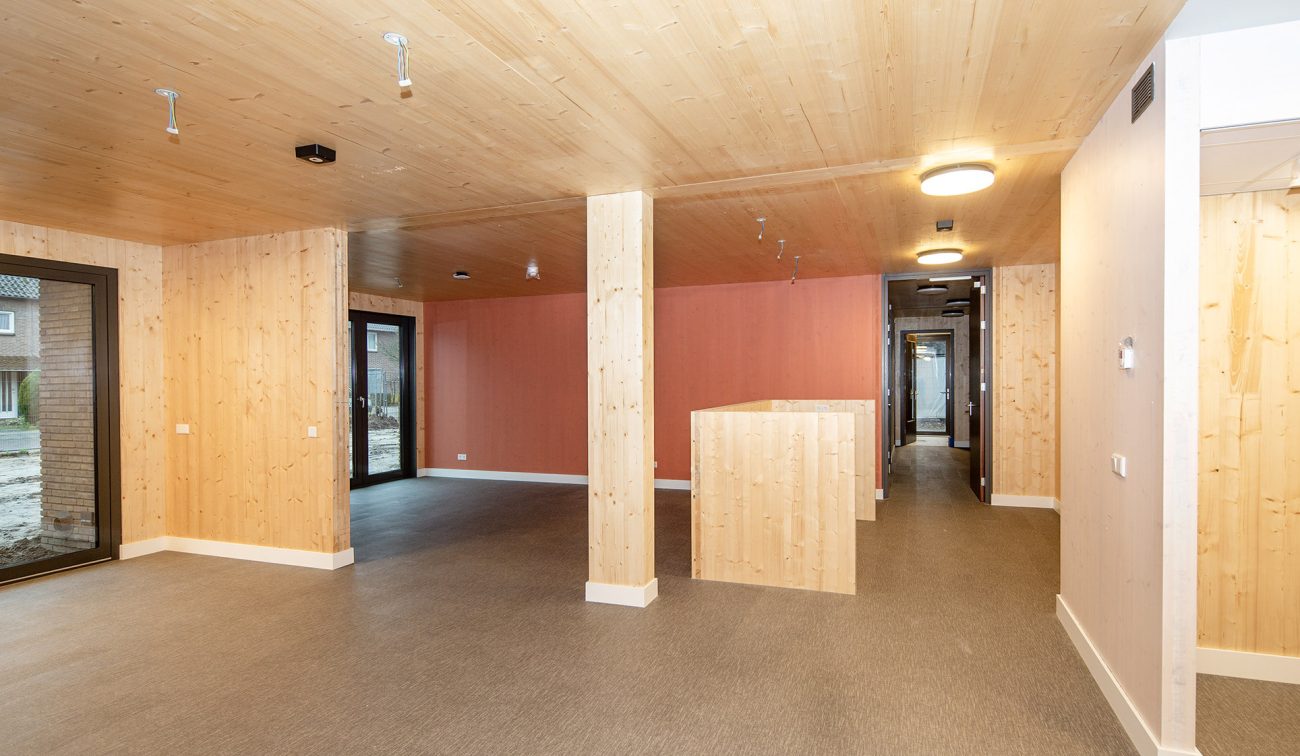 Interieur van het woonzorgcomplex Pontenage in Gemert, met houten wanden en plafonds, warme verlichting en een open indeling met zicht op de gang en grote ramen.
