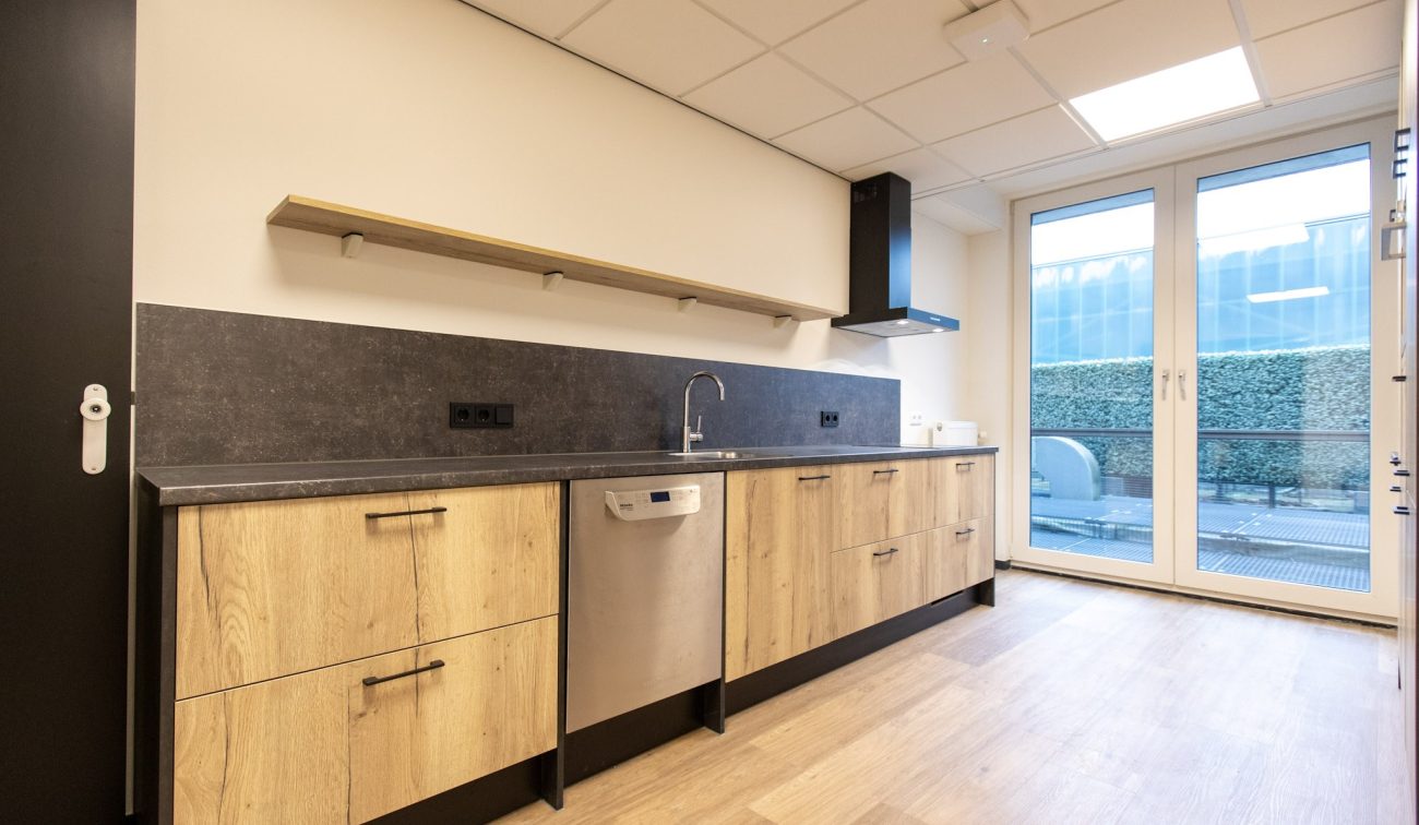 Zorghuis-gang met grote ‘1’, open deur naar keuken en zitje met twee stoelen en tafeltje