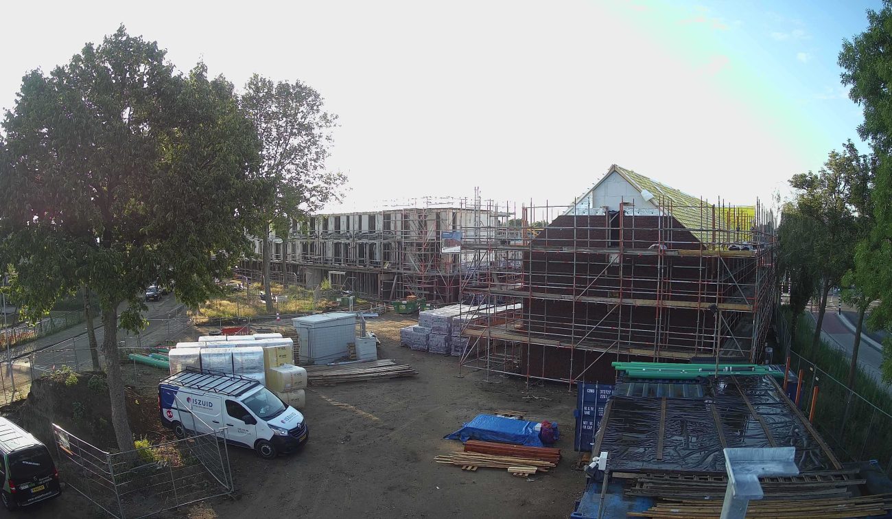 Nieuwbouw Emmalaan Roermond – bouwplaats met rijwoningen in steigers, dakbeschot in aanleg en stapels bouwmateriaal; bestelbus op terrein