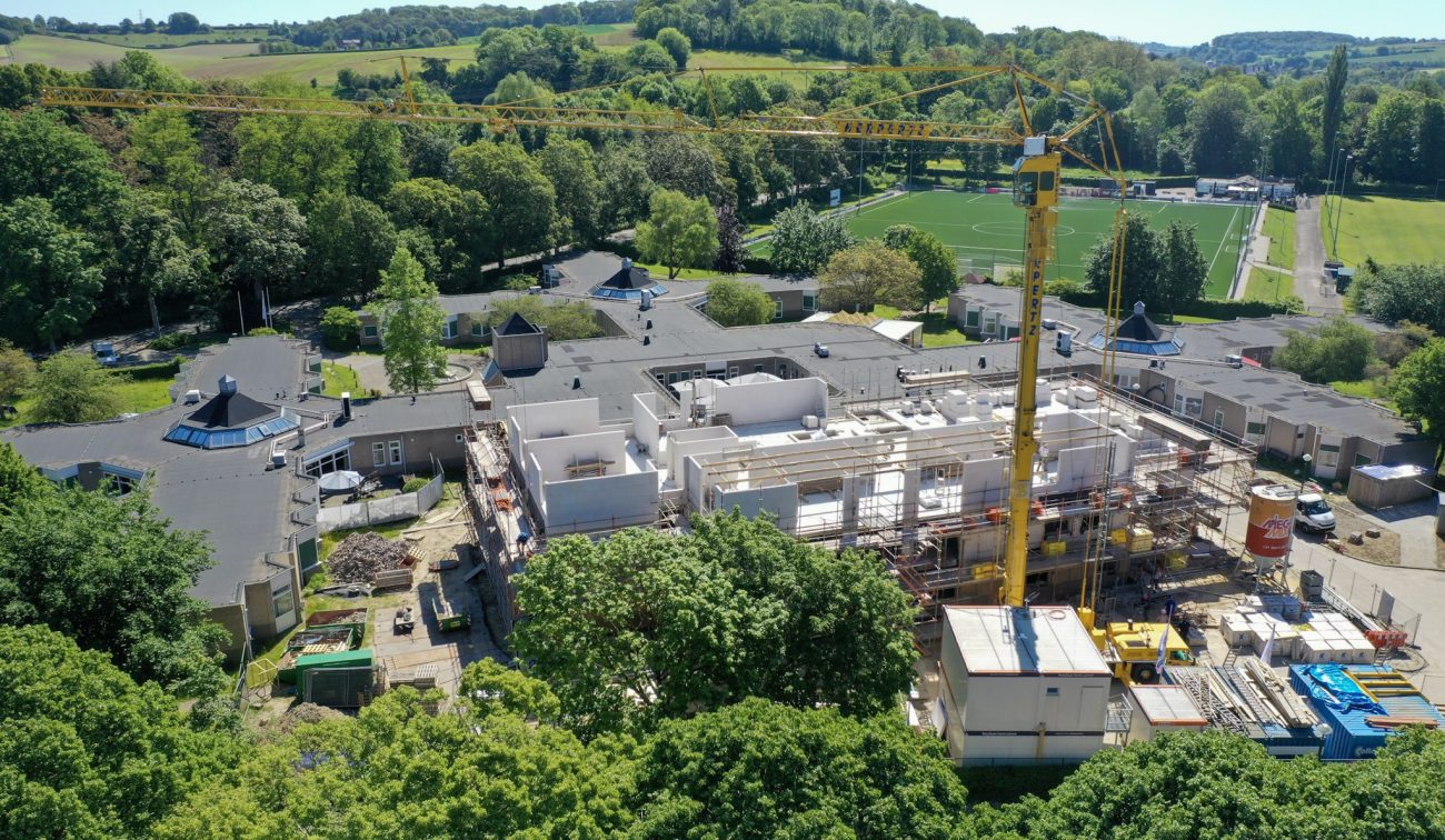 Nieuwbouw zorgcomplex Valkenburg, casco in opbouw met gele torenkraan en sportpark.