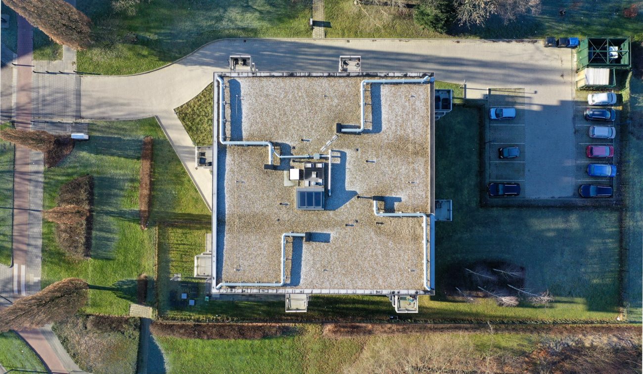 Luchtfoto dak nieuwbouw Noorderkroon Brunssum – plat grinddak met installaties en lichtkoepel, parkeerplaats en groenvoorziening eromheen