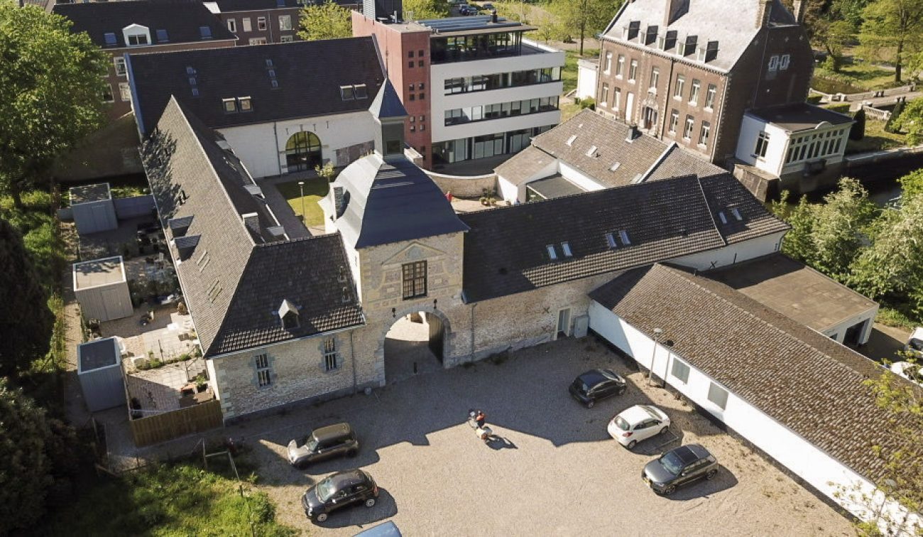Monumentale hoeve met toegangspoort, leien daken en geparkeerde auto’s op binnenplaats — transformatie naar appartementen in Maastricht