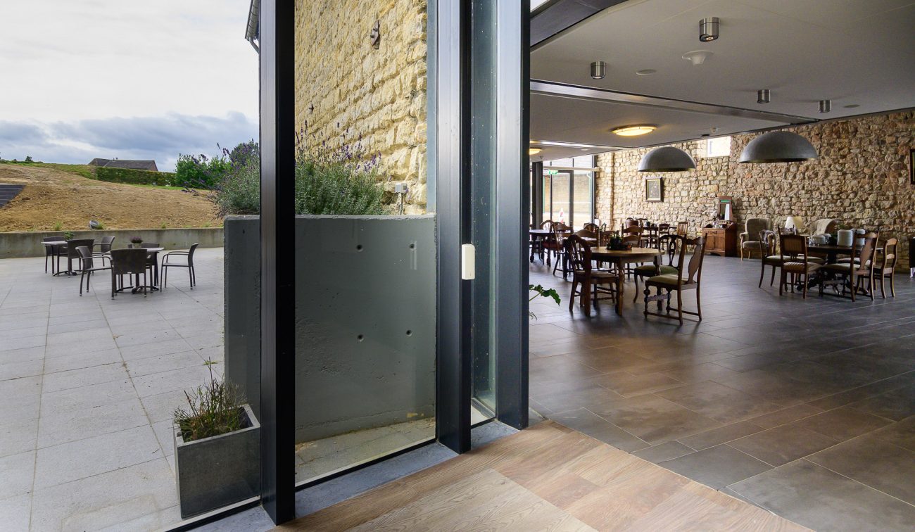 Interieur hoeve Overhuizen met historische mergelmuur, openslaande glazen pui naar terras.