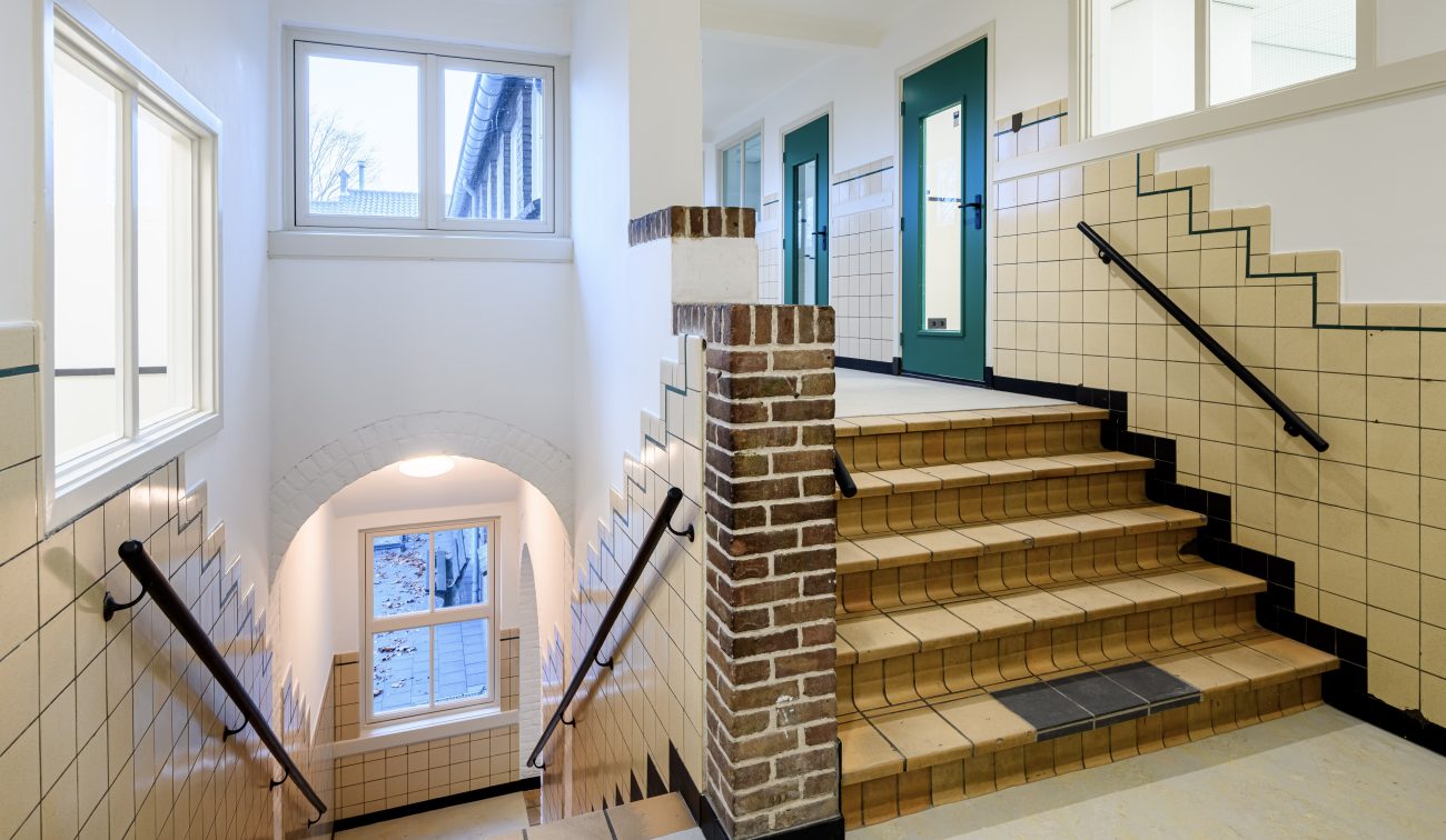 Monumentaal interieur: tegeltrap met contrasterende zwarte stootranden en groene deurkozijnen.