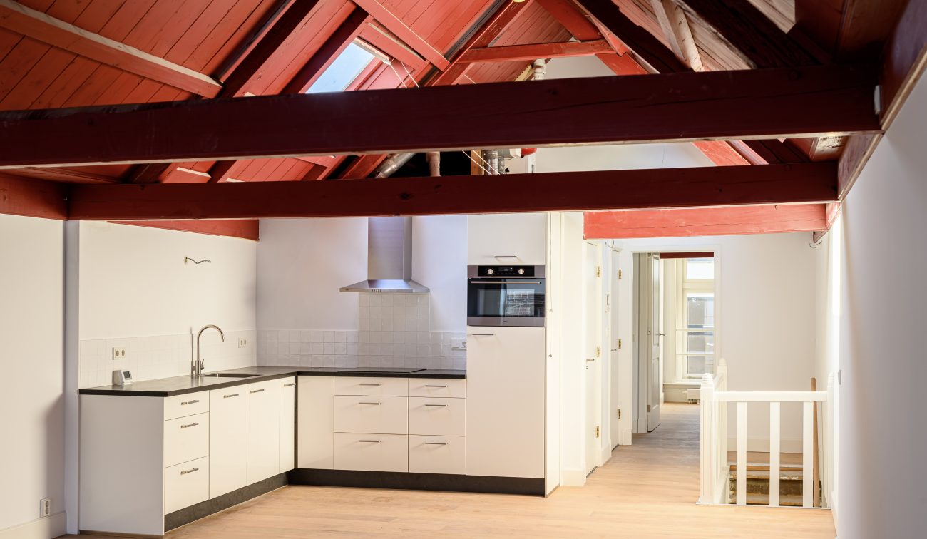 Transformatie Lijnmarkt & Visschersplein Utrecht – zolderappartement met open keuken en roodhouten spanten.