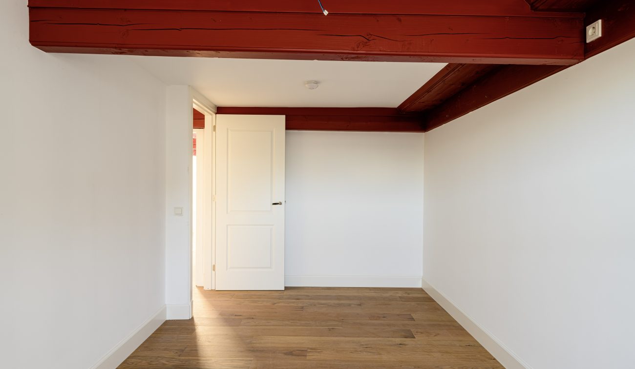 Transformatie Lijnmarkt & Visschersplein Utrecht – slaapkamer met zichtbare rode balken, witte wanden en houten vloer.