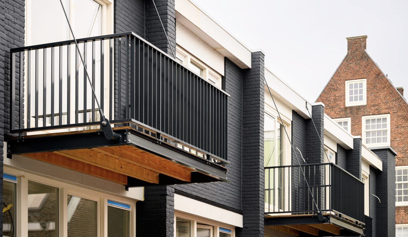 Transformatie Lijnmarkt/Visschersplein: stalen balkonconstructies aan zwarte baksteen, wit kozijnwerk.