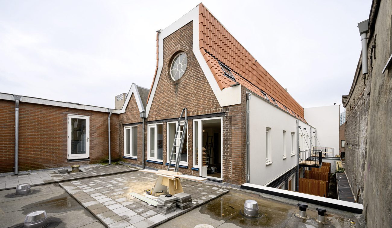 Renovatie aan Lijnmarkt/Visschersplein: dakterras met ladder, rode kap en rond raam in bakstenen top.