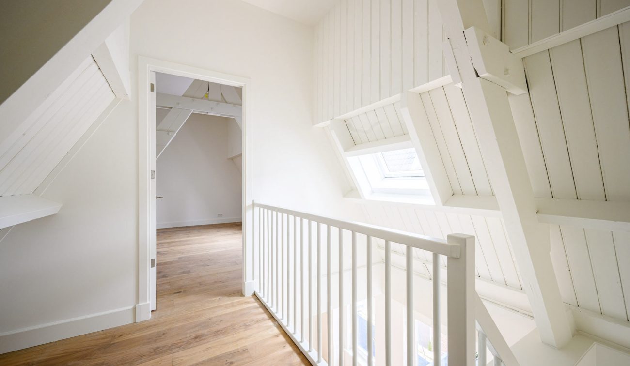 Transformatie Lijnmarkt & Visschersplein Utrecht – lichte overloop met witgeschilderde kapconstructie, dakraam en houten vloer, met doorkijk naar slaapkamer.