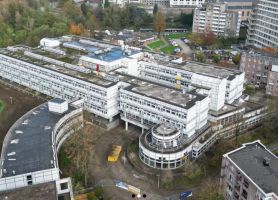 Kloosterbeemden Kerkrade – luchtfoto van groot wit gebouwcomplex met terrassen en ronde entree, omgeven door woonblokken en groen