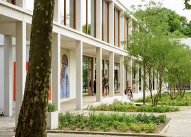 Overdekte looproute langs glazen puien; leerlingen pauzeren tussen jonge bomen en borderplanten.