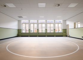 Lichte gym-/multizaal met mintgroene lambrisering, hoge ramen en cirkelbelijning op de vloer