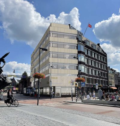 Gevel van een kantoorpand midden in een stad met blauwe lucht en bewolking