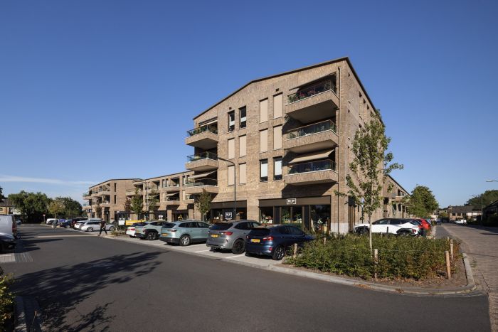De Scheperij Teteringen: hoekgebouw met balkons, baksteen, winkels; straatbeeld, geparkeerde auto’s.