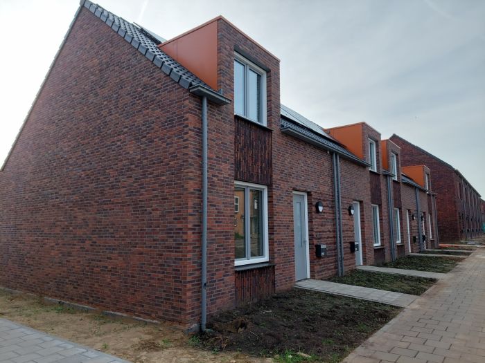 Nieuwbouw Bredeweg Roermond – rijwoningen in roodbruin metselwerk met witte kozijnen en oranje dakkapellen, stoep en voortuinen