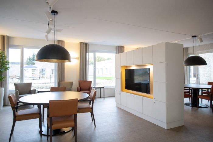 Gezamenlijke woonruimte verpleeghuis Panhuys Hulsberg met ronde tafels en grote hanglampen.