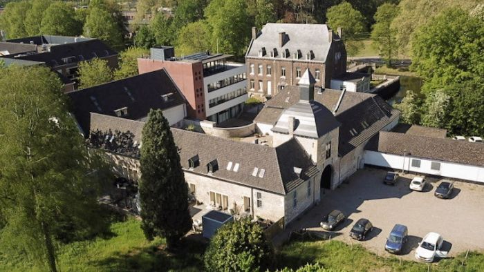 Luchtfoto van historische carréhoeve met poortgebouw en binnenplaats, naast moderne appartementen — herbestemming tot woningen in Maastricht.