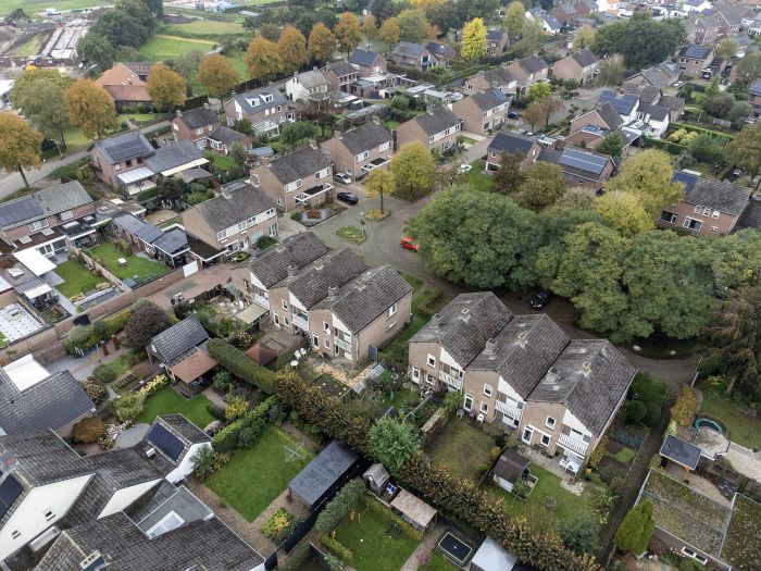 Luchtfoto van een woonbuurt in Stramproy: rijen rijwoningen en twee-onder-een-kap met achtertuinen, veel groen en enkele zonnepanelen—locatie voor groot onderhoud aan 28 woningen.