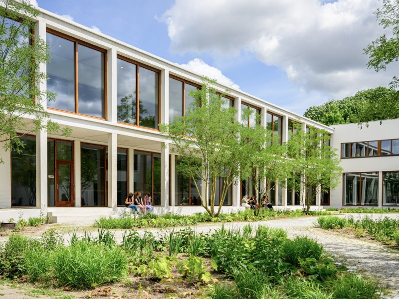 Transparante onderwijsgevel met veranda langs de patio; leerlingen relaxen tussen het groen.