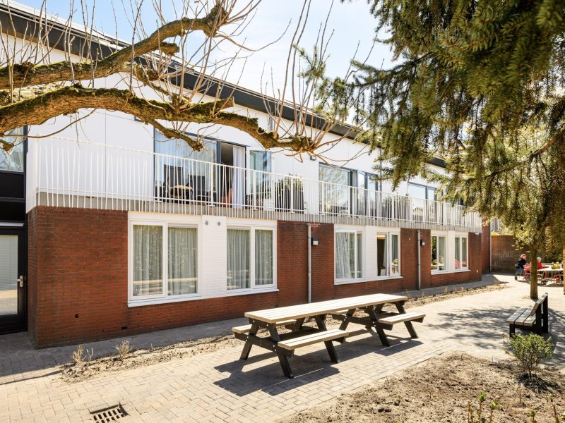 Renovatie en optopping Plataanlaan Baarn: woongebouw met balkonhekken, baksteen, tuin en oude bomen.