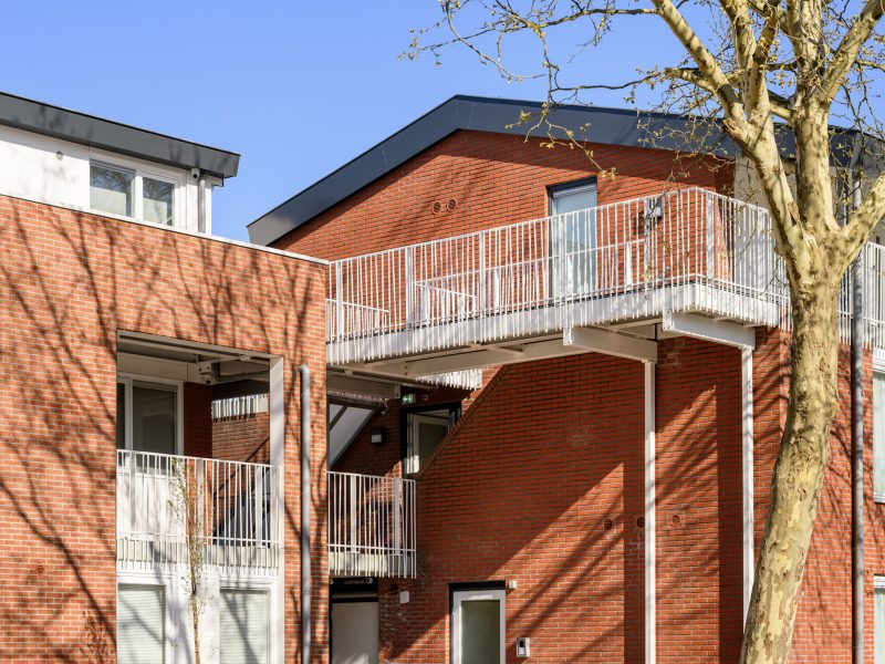 Renovatie Plataanlaan Baarn: rode baksteen witte galerijen en loopbrug en nieuwe gevels en kozijnen.