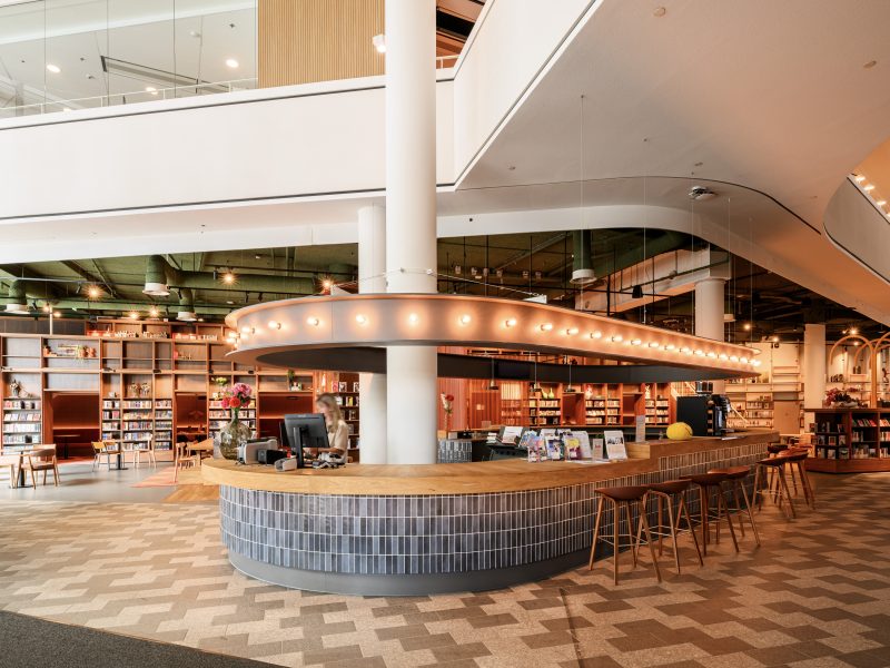 Moderne ontvangstzone met tegelbalie, brochures en open boekenkastruimte.
