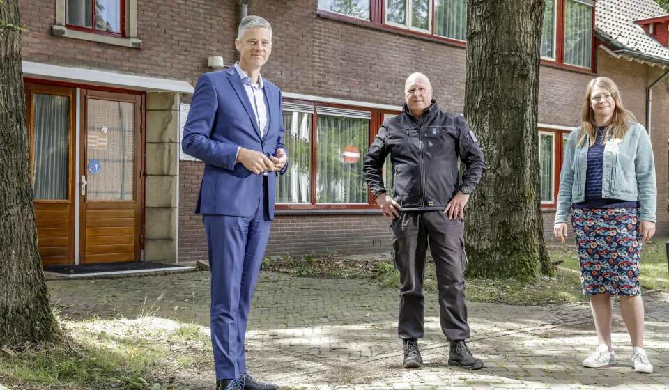 Drie personen voor bakstenen woongebouw met rode kozijnen en volwassen bomen